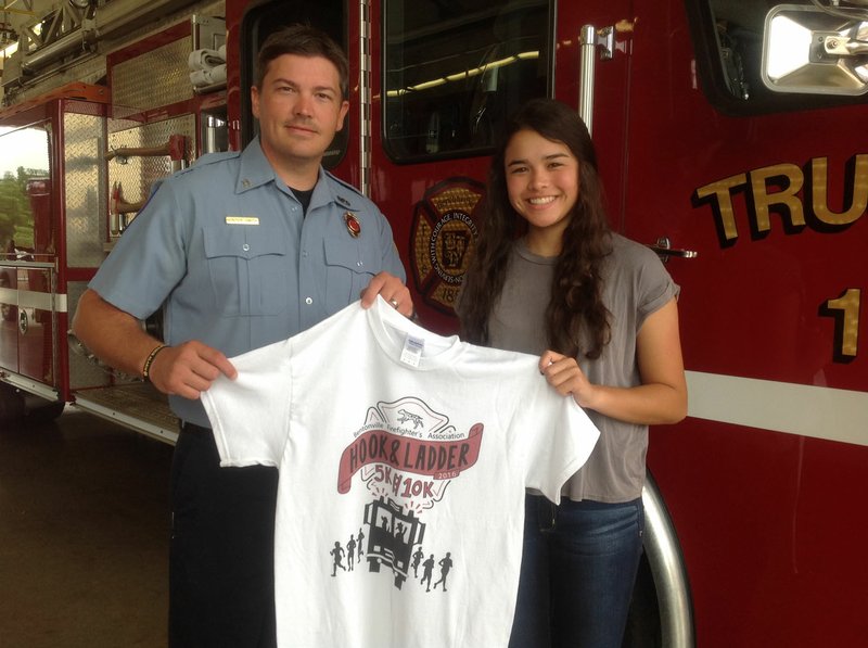 Bentonville Fire Department Capt. Hunter Smith and Kirstyn Tureman hold a T-shirt Tureman designed for the Bentonville Firefighter’s Association’s first Hook & Ladder 5k/10k race, to be held Aug. 6. Tureman’s design was chosen the winner in a contest the association made available to Bentonville High School students.