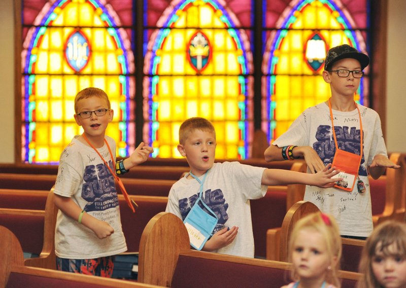 Truman Wheeler, 7, (from left) Hollister Unruh-Poteet, 7, and Benjamin Wheeler, 10, dance as they do “energiz er” exercises to start their vacation Bible school session Wednesday at First Presbyterian Church in Springdale. 