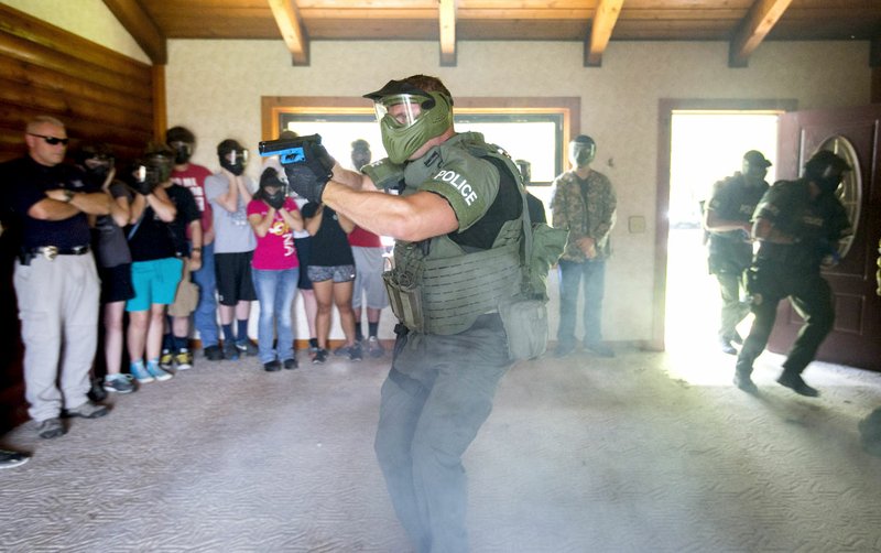 Participants in the Bentonville Police Youth Academy watch as Cpl. Brent Farrer (near) and other members of the squad’s SWAT team move into position on Friday during training inside an abandoned house in Bentonville.