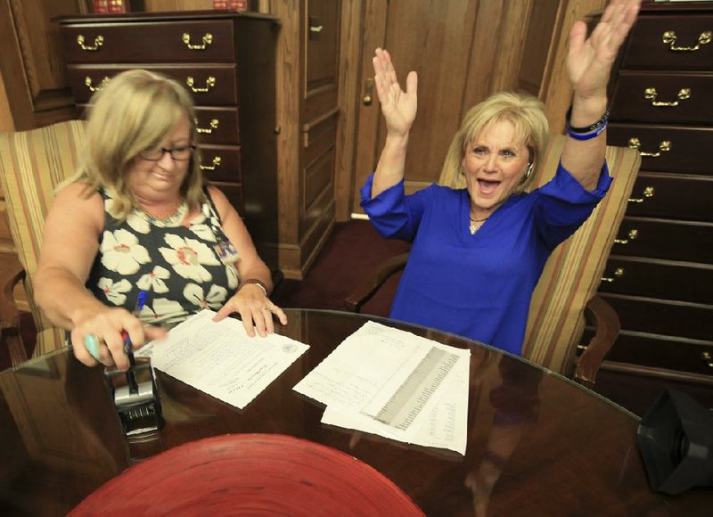 Arkansans for Compassionate Care campaign director Melissa Fults (right) celebrates as Leslie Bellamy of the secretary of state’s office stamps paperwork for petitions that Fults’ group delivered in June in hopes of getting a medical-marijuana initiative on the ballot.