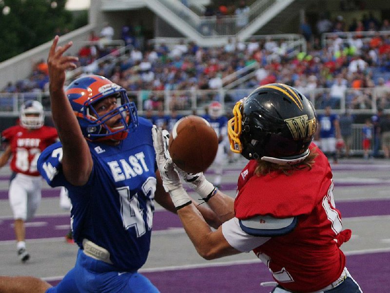 The West’s Adriene Lasko (right) catches a pass in front of the East’s Zack Powell during Friday night’s high school All-Star football game at Estes Stadium in Conway. The West jumped out to a 21-0 lead to roll past the East 31-21.