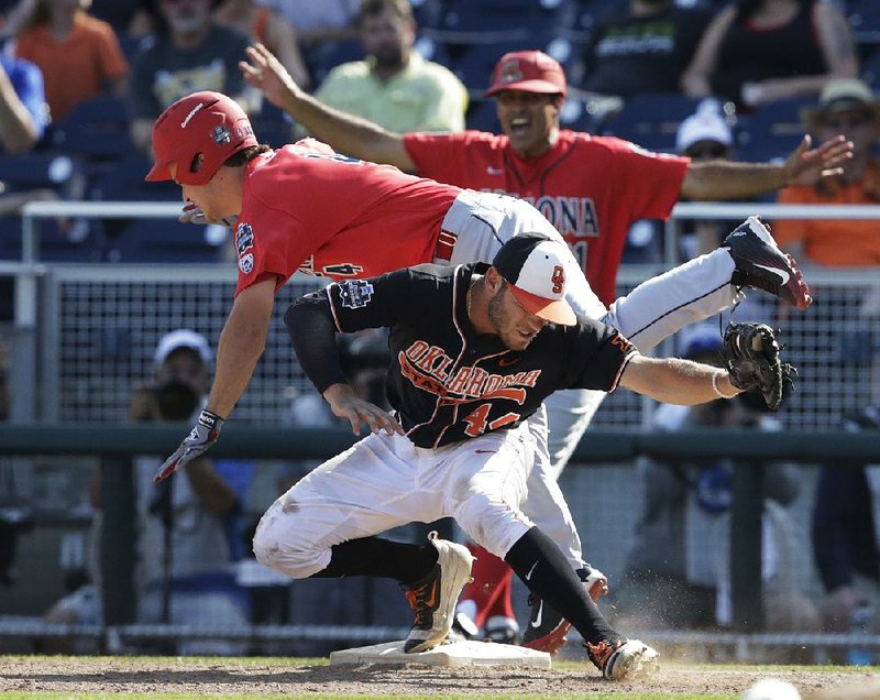 Arizona’s Justin Behnke (back) is safe at first base after colliding with Oklahoma State’s Andrew Rosa in the ninth inning of Friday’s game at the College World Series. The Wildcats moved a step closer to advancing to the championship series after beating the Cowboys 9-3.