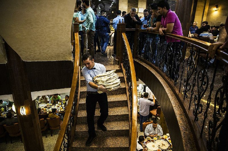 A waiter carries a stack of kebabs wrapped in bread as the fast-breaking evening meal gets underway on a recent day at the Haji Hussein restaurant in Baghdad. 