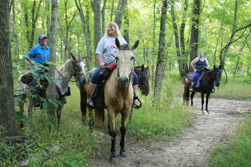 Susan Sullivan (from left) and Angie King of Fayetteville and Lee Ann Dedmon of Lowell share a laugh Wednesday during an evening horse ride on one of Lake Sequoyah’s equestrian trails in Fayetteville. Fayetteville’s Parks and Recreation Advisory Board this month voted to permanently allow horses on several miles of trails on the lake’s west side.