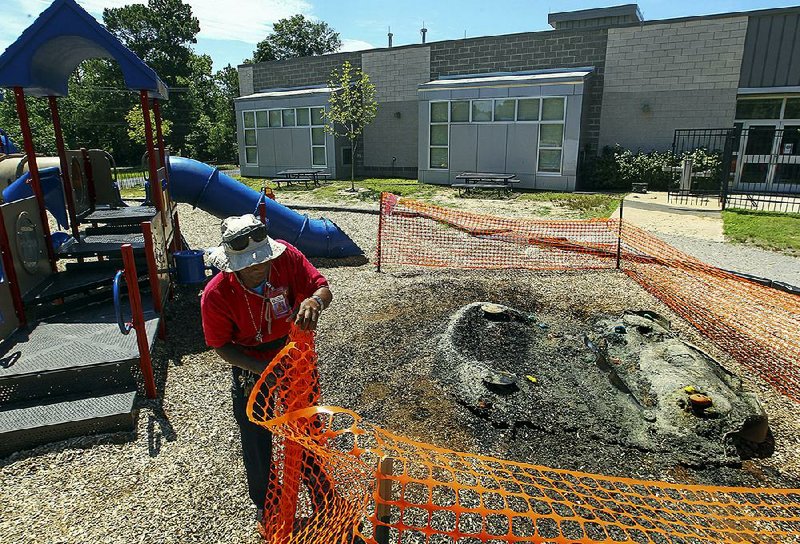 Little Rock School District worker Randy Chapman installs a temporary barrier around a burned plastic climbing wall on the playground of Chicot Primary School. The overnight fire, which destroyed part of the playground, is the second fi re on a Little Rock school playground this month.