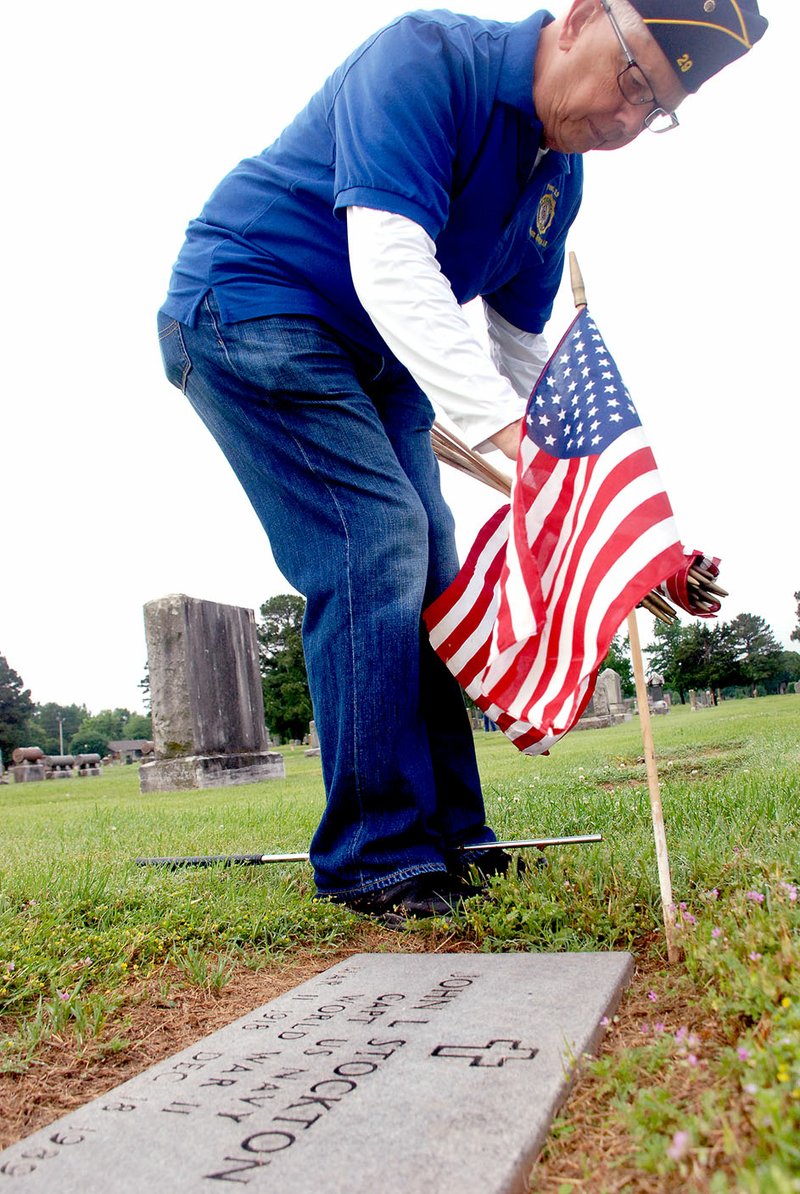 Jeff Della Rosa/Special to Siloam Proud Jerry Cavness of Siloam Springs places a flag at the headstone of U.S. Navy Capt. John Stockton, a World War II veteran. Cavness, who served in the military during the Vietnam War, recently joined American Legion Post 29 and is a member of its honor guard.