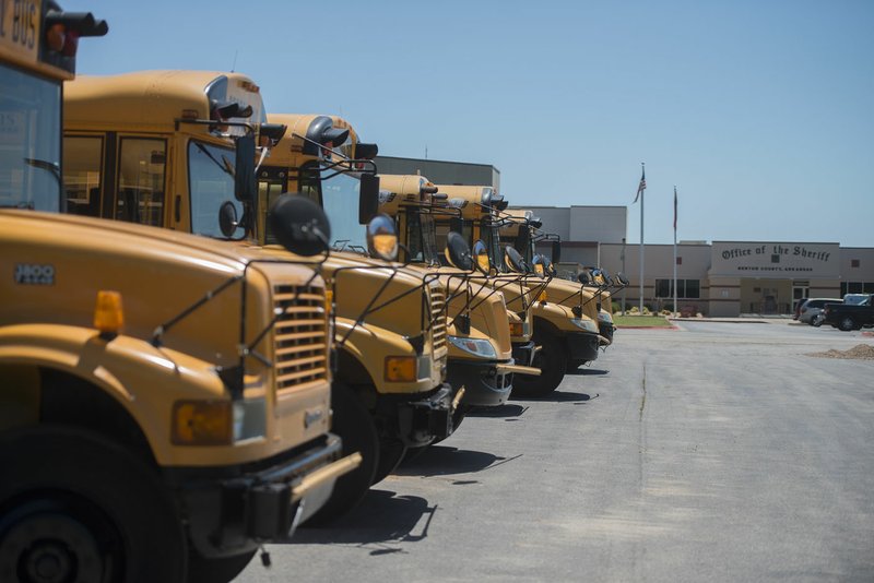 Eight Bentonville School District school buses line up Tuesday at the Benton County Sheriff’s Office in Bentonville. County work crews are cleaning the entire fleet for the district.