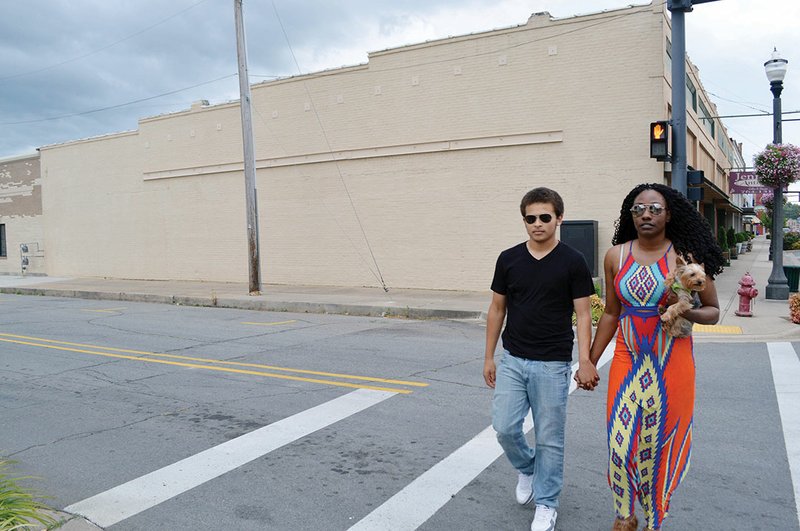 Brontez Harris of Morrilton and Tyresha Byers of Cleveland, holding her Yorkie, Bentley, walk across the crosswalk at Oak and Court streets in downtown Conway. The blank wall on Court Street, the east side of Jenifer’s Antiques, is one possibility for an endangered-species mural that the Center for Biological Diversity may fund. The Conway Public Art Board is helping with the proposal.