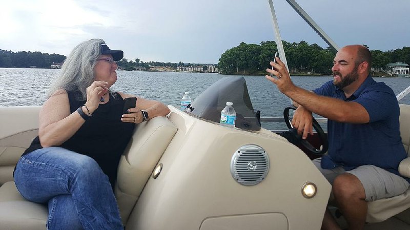 Corey Boelkens (right), creator of RaftUp, shows points of interest using an app on his phone to fellow entrepreneur Alese Stroud on Lake Hamilton in Garland County. 