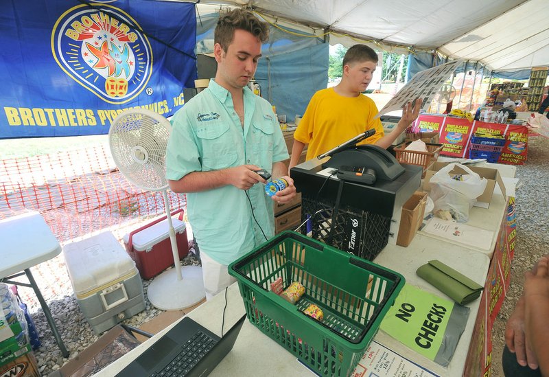 Ben Kueter (left) and Jeron Tull, check out customers Wednesday at Jake's Fireworks on South West End Street across from St. Raphael Catholic Church in Springdale. Some firework tent operators are concerned about safety in the wake of an armed robbery of a tent last year.
