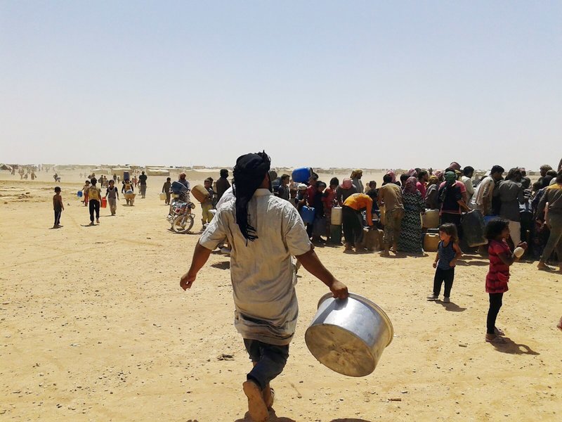 In this Tuesday, June 28, 2016 photo, Syrian refugees gather for water at Ruqban border camp in northeast Jordan. Syrian refugees and international aid officials say little water and no food has reached 64,000 Syrian refugees stranded in the desert since Jordan sealed its border in response to a suicide attack on June 21, 2016.