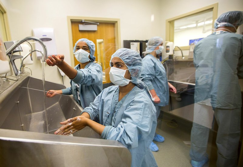 Pooja Naik (left), 17, and Namrata Gopinath, 16, both of Bentonville, wash their hands Friday before entering an operating room at Mercy Hospital in Rogers.
