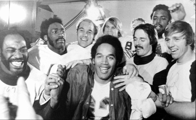O.J. Simpson is surrounded by teammates in the Buffalo Bills locker room at New York’s Shea Stadium in December 1973 after setting a new NFL single-season rushing record. Teammates from left are Reggie McKenzie, J.D. Hill, Joe DeLamielleure, Paul Seymour, Bob Chandler, Don Green and Joe Ferguson.