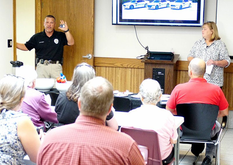 Photo by Randy Moll Keith Smith, Gentry police chief (left), speaks briefly to a group of business leaders at the police department&#8217;s open house on June 23. Also addressing the group was Janie Parks, director of the Gentry Chamber of Commerce (right).