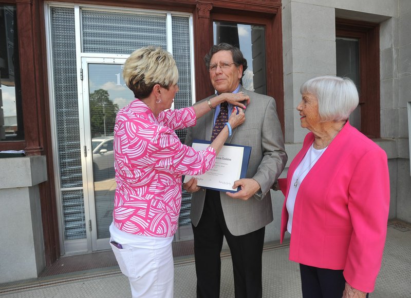 Frances Rankin (left) and Wanda Bautts, (right) both with the James Bright Chapter of the National Society Daughters of the American Revolution, presents John Mack from JKJ Architects the Historic Preservation Medal from the society’s Historic Preservation Committee on Tuesday in front of the old First National Bank building in downtown Rogers. The national award recognized Mack for his effort restoring several historic buildings in the area.