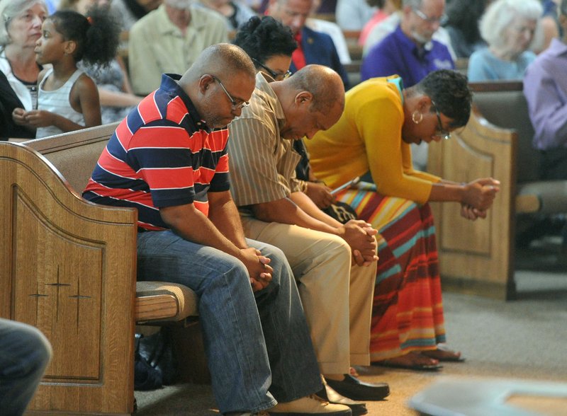 Curtis Smith, (left) senior pastor at St. James Missionary Baptist Church in Fayetteville, joins with others Friday during a prayer vigil to promote peace and unity and support for the families of the victims of the recent shootings in Baton Rouge, La., St. Paul, Minn., and Dallas. The vigil at St. James in Fayetteville was attended by several Northwest Arkansas religious leaders and residents.