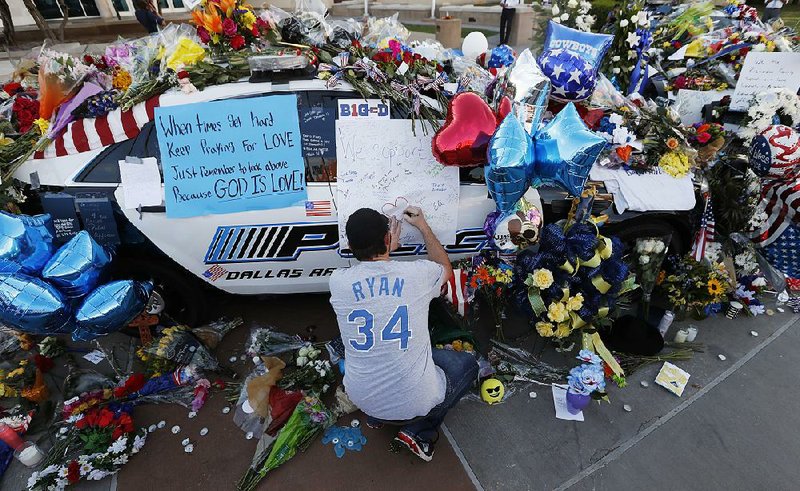 Tracy St. Romain leaves a note Saturday outside the Dallas Police Department headquarters on a patrol car that has become a makeshift memorial for the five slain Dallas law enforcement officers. 