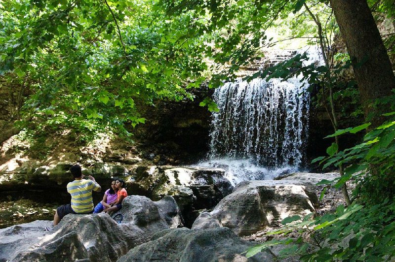 A family enjoys the cool rocks below the falls on Bella Vista’s Tanyard Creek Nature Trail.
