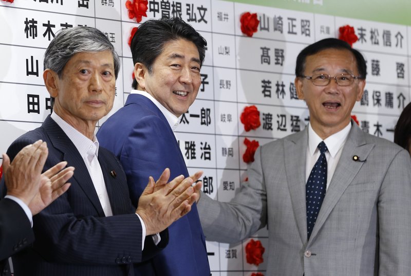Japanese Prime Minister Shinzo Abe (center) smiles Sunday as he places a red rosette on the name of his Liberal Democratic Party’s winning candidate during ballot counting for the parliamentary upper house elections at the party headquarters in Tokyo.