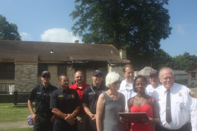 Monica Walters stands with North Little Rock Alderman Beth White and members of the police and fire departments after receiving recognition for her actions helping alert neighbors about a fire in their building. 