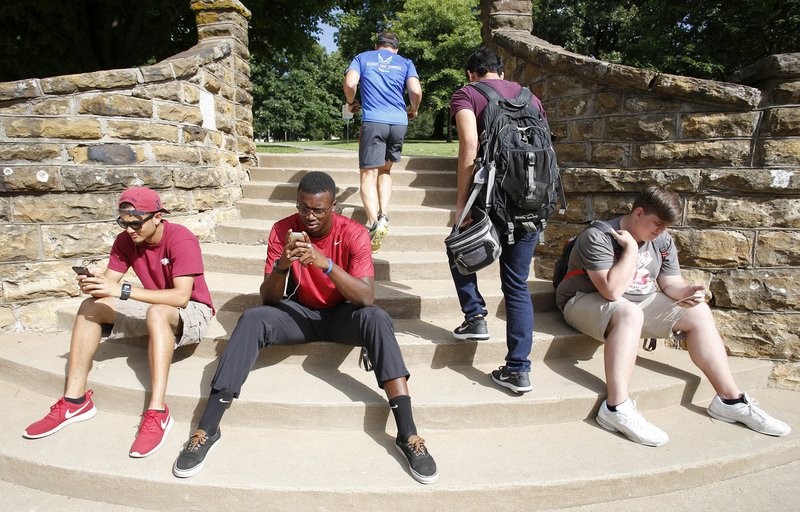 Pedestrians walk Wednesday up the steps through Stephen Payne (from left), a recent graduate from the University of Arkansas; Larry Donald, a senior; and Max Sanderlin, a recent graduate, as the three attempt to capture Pokemon at a Pokemon Stop at the intersection of Arkansas Avenue and Dickson Street in Fayetteville. The three are playing Pokemon Go, a location-based reality mobile game.
