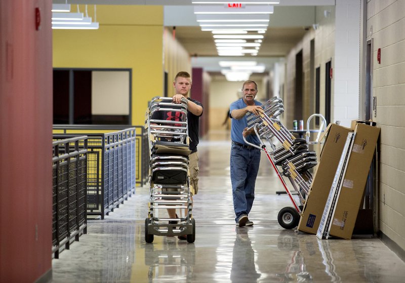 Dalton Nesbitt (left) and Norm Simpson, both with Rogers-based Moser Corporation, move chairs Friday for the art drafting classroom at West High School in Centerton.