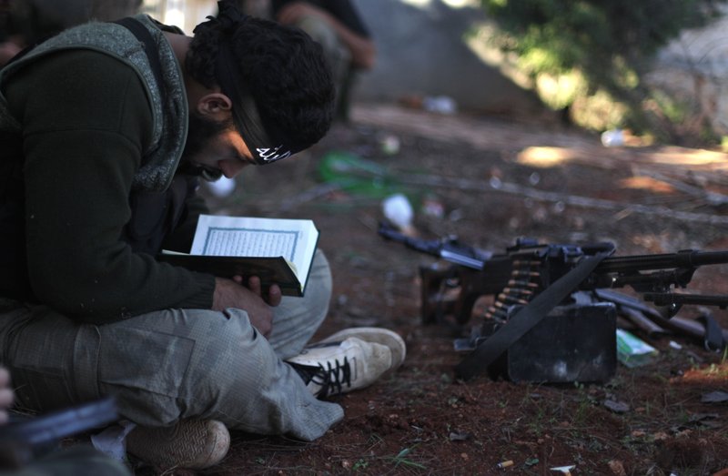 In this Nov. 15, 2012 file photo, a Syrian rebel reads Quran during clashes with government forces in Aleppo, Syria. Syrian opposition activists said Sunday, July 17, 2016 that government forces and their allies have closed the only road leading into and out of rebel-held parts of the northern city of Aleppo, besieging hundreds of thousands of people. 