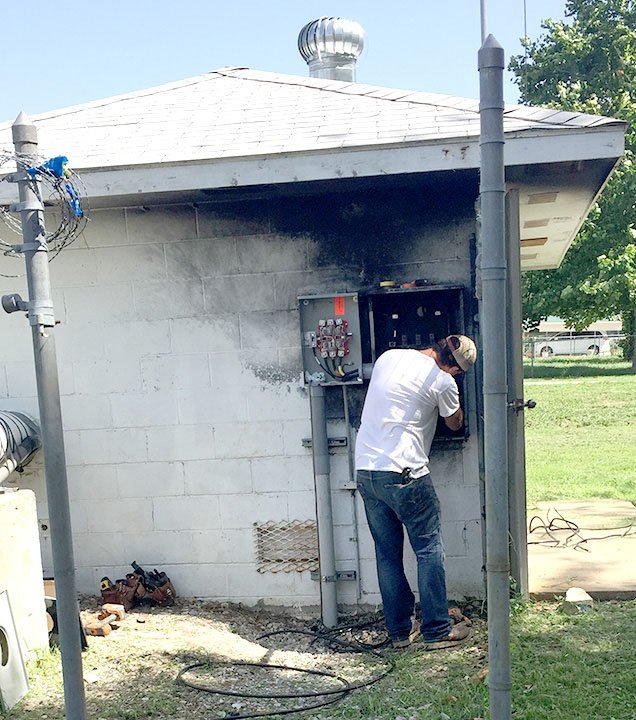 Submitted Photo A Decatur city worker rewires a new junction box into the pump relay system after a lightning strike put City Well Number 3 out of commission for a short time July 11. The black marks above the worker show where the lightning bolt burned the paint off of the cinderblock building.