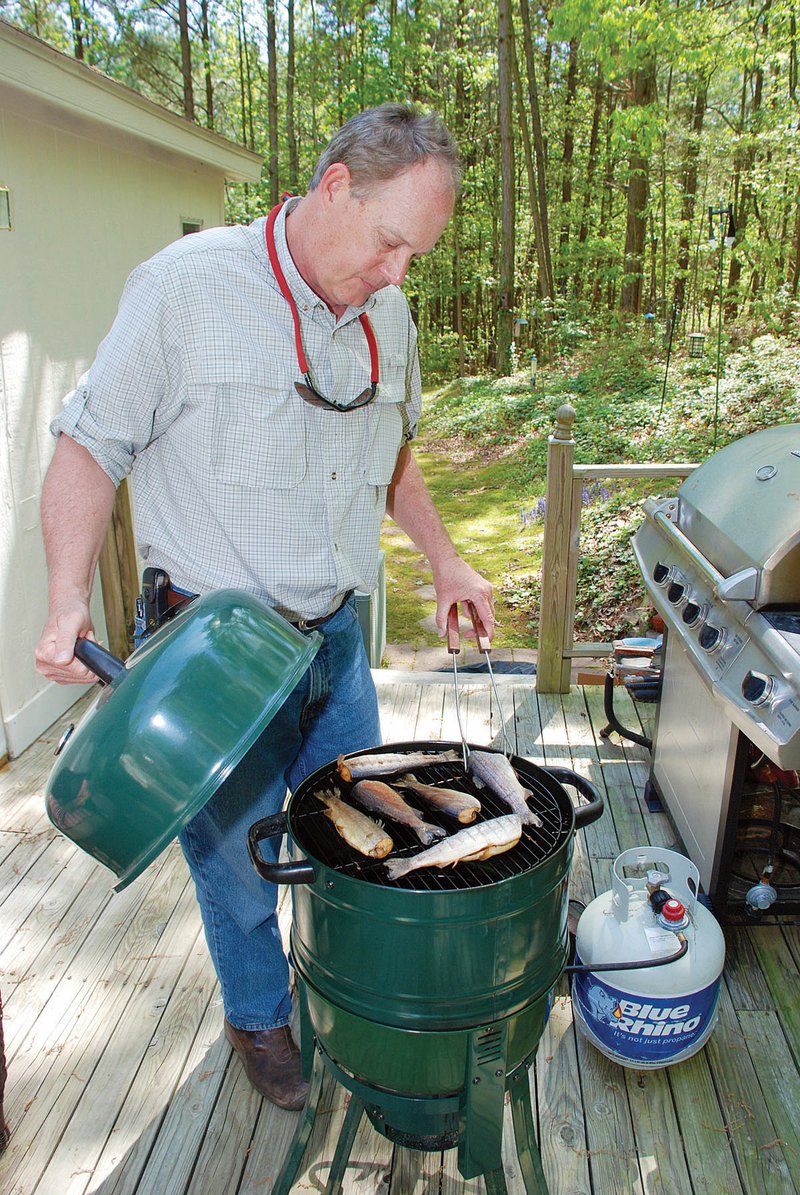 Gregg Patterson of Little Rock uses a water smoker to prepare a delicious meal of trout caught in the Little Red River. Soaked wood chips create smoke that adds flavor to the fish.