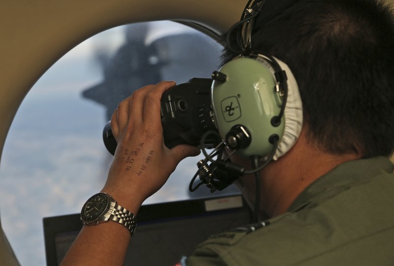 FILE - In this March 22, 2014, file photo, Flight Officer Jack Chen uses binoculars at an observers window on a Royal Australian Air Force P-3 Orion during the search for missing Malaysia Airlines Flight MH370 in Southern Indian Ocean, Australia. The hunt for Malaysia Airlines Flight 370 will be suspended once the current search area in the Indian Ocean has been completely scoured, the ministers of the three countries conducting the operation announced Friday, possibly ending all hopes of solving aviation's greatest mystery. (AP Photo/Rob Griffith, File)
