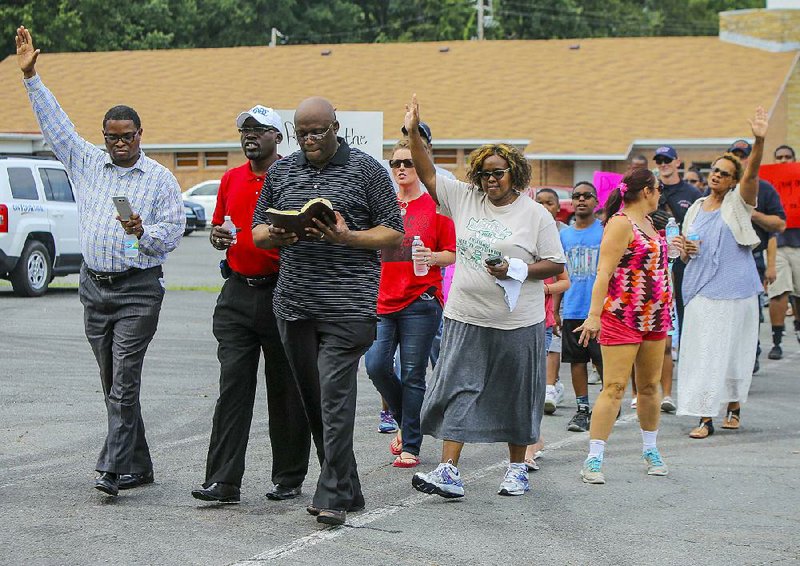 The Rev. Robert Robinson (front, with Bible) leads a group of marchers in responsive readings from the Bible as they conduct a community prayer walk along Chicot Road in Little Rock on Sunday afternoon.

