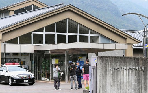 A police officer talks with visitors in front of a facility for the disabled where a number of people were killed and dozens injured in a knife attack Tuesday, July 26, 2016, in Sagamihara, outside Tokyo. 