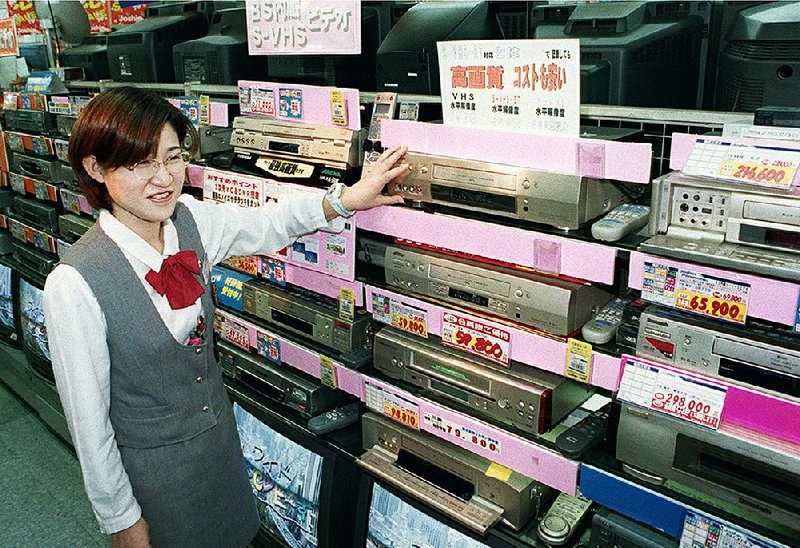 A salesclerk shows high quality VHS videocassette recorders at an electronics store in Osaka, Japan in this 1998 file photo. Osaka-based Funai Electric Co., the last maker of VCRs, said Monday that production will end this month.