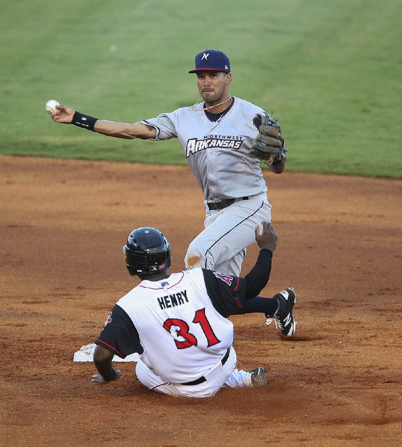 Northwest Arkansas Naturals shortstop Humberto Arteaga throws - over Arkansas Travelers baserunner Jabari Henry to complete. a double play during Tuesday night’s game at Dickey-Stephens C Park in North Little Rock. The Travelers won 2-1.