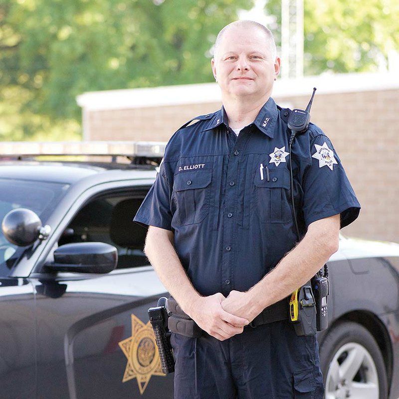 Officer Dalton Elliott of the Mayflower Police Department stands near a patrol car after he ends a shift. Elliott was hired as the full-time school resource officer for the Mayflower School District, and he will drive a 2015 Dodge Charger that is getting decals with the Eagle mascot, as well as names of donors. Elliott, 44, has four children in the school district.