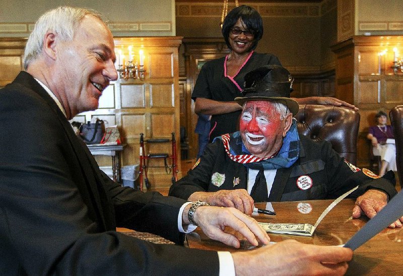 FILE — In this 2016 file photo, Jess "Woody" Woods, clad in his clown attire, gets a laugh out of Gov. Asa Hutchinson at the Capitol during the signing of a proclamation naming the first week in August as International Clown Week.