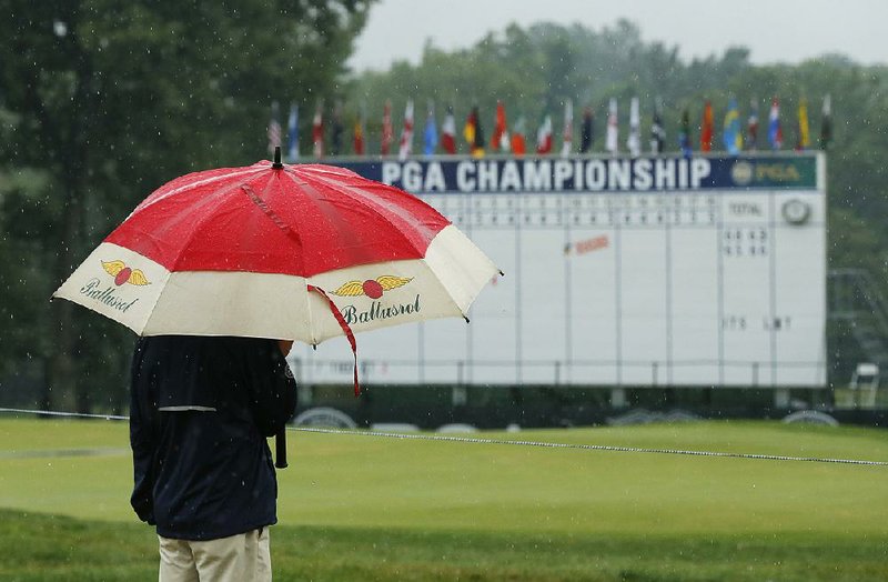 A fan stands near the 18th hole during a rain delay Saturday at the PGA Championship. Third-round play was suspended after thunderstorms and heavy rain soaked the Baltusrol Golf Club. Only 37 players were able to complete the round, which is scheduled to resume today at 6 a.m., but more rain is in the forecast.