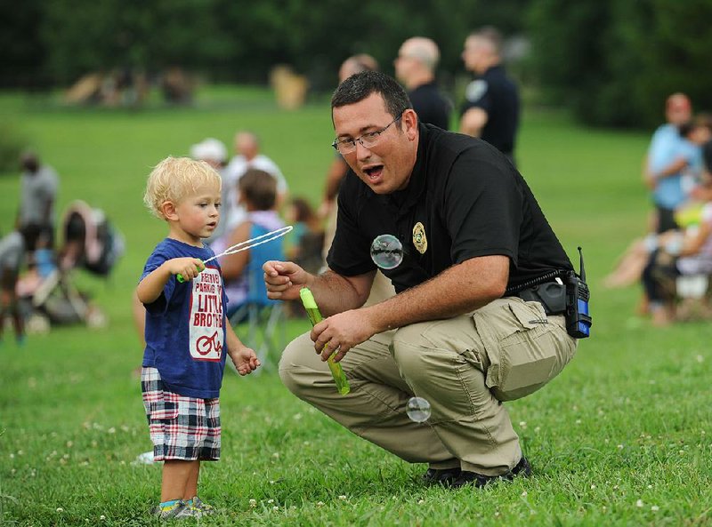 Cpl. Thomas Reed of the Fayetteville Police Department smiles Saturday as he blows soap bubbles with Thomas Peace, 2, of Fayetteville during NWA CommUNITY Cares, a gathering of community members, police and government representatives organized by Nice-US, in Gulley Park in Fayetteville.