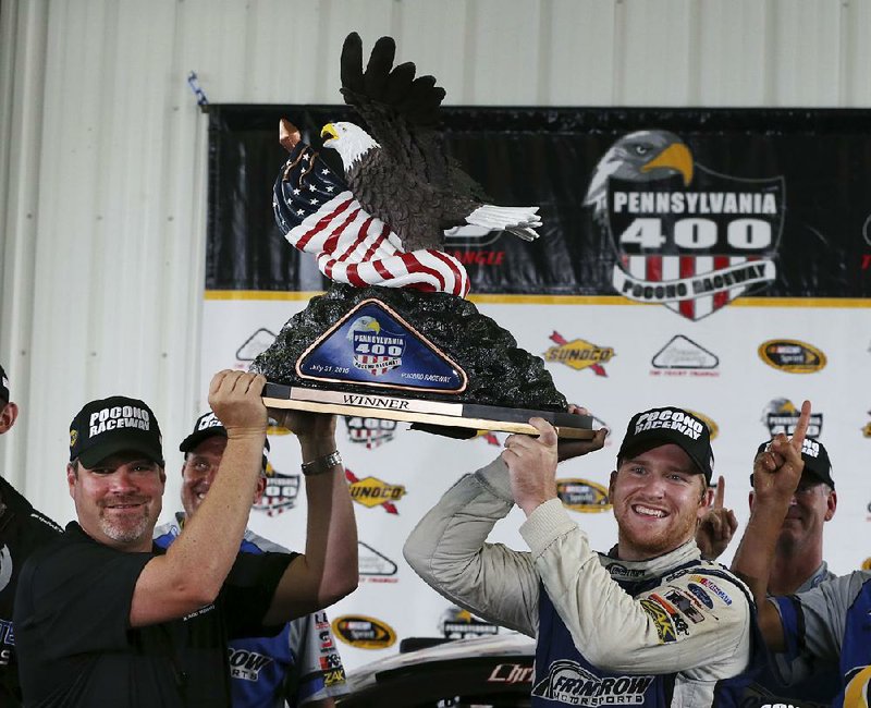 Chris Buescher (right) holds up the winner’s trophy with the help of Pocono Raceway President Brandon Igdalsky after winning the fog-shortened Pennsylvania 400 on Monday at Pocono Raceway in Long Pond, Pa.