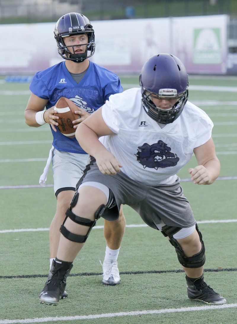 Fayetteville High School quarterback Taylor Powell takes a snap under center from Max Thurman Monday, August 1, 2016, during practice at Harmon Stadium in Fayetteville. The Fayetteville High School Football team is now being coached by first year head coach Bill Blankenship.