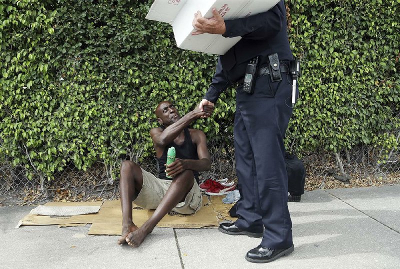 Lorenzo Ward, 45, who is homeless, shakes hands with Miami police officer James Bernat after Bernat gave him a can of insect repellent Tuesday in the Wynwood neighborhood of Miami.