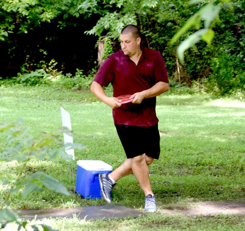 Photo by Mike Eckels Mike Stout tees off on hole number 9 at the Old Town Park disc golf course in Gravette July 30. Stout, disc golf course designer and builder, was part of the first annual Decatur-Gravette Disc Golf tournament at Decatur Veterans and Gravette Old Town Parks.