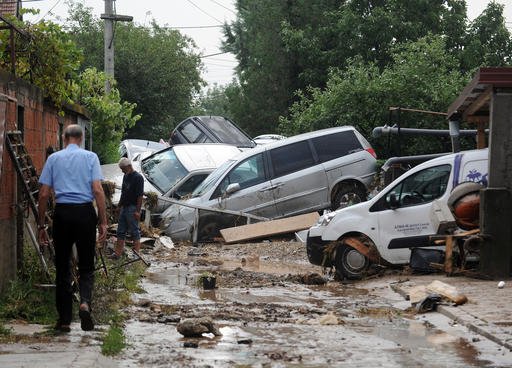 People walk through a street where cars have piled due to overnight flooding after storms in the village of Stajkovci, just east of Skopje, Macedonia, on Sunday, Aug. 7, 2016.