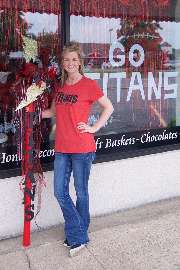 Lauren Martin, who is over sales and marketing at Double R Florist & Gifts, poses with the handmade spirit stick that store employees created in support of the city’s Paint the Town Red event to show school spirit for the Jacksonville North Pulaski School District.