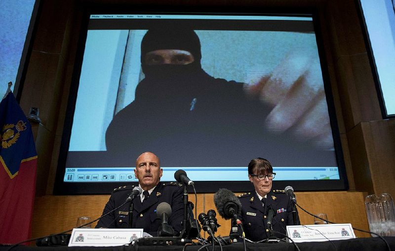 A video of Aaron Driver is seen behind Mike Cabana and Jennifer Strachan, commanders of the Royal Canadian Mounted Police, as the two talk Thursday in Ottawa about the operation to thwart Driver’s bombing plot. Driver was killed. 