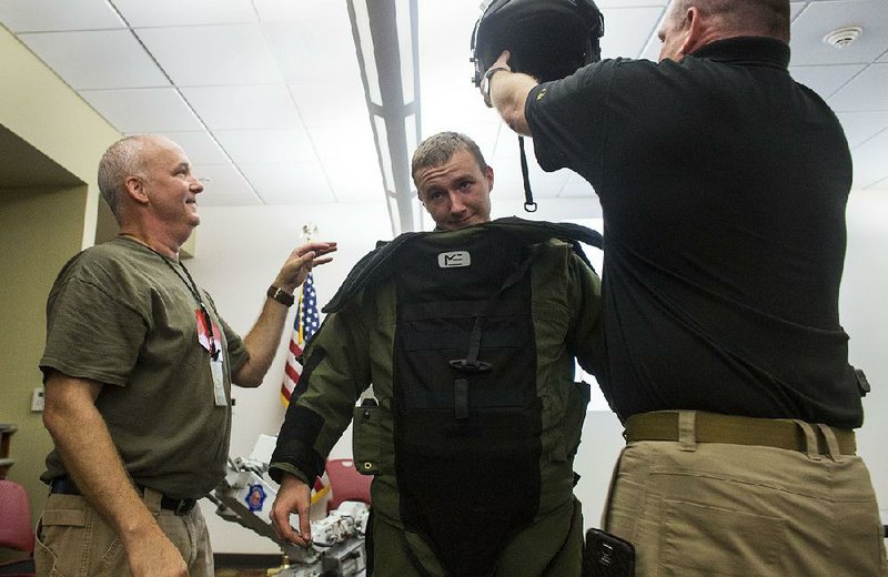 Jackson Stepp, 17, a junior at Springdale High School, gets suited up in bomb squad protection gear during a presentation by Sgt. Mike Dawson (left), bomb squad commander with the Arkansas State Police, and special bomb squad technician Joel Eubanks (right) on Thursday at the Arkansas Department of Emergency Management. 