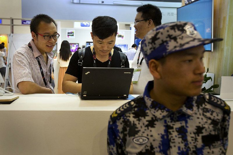 Visitors use a laptop computer at a display booth as a security guard stands nearby at the 2015 Global Mobile Internet Conference in Beijing.