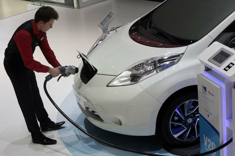 An employee prepares to install a charging plug in the socket of a Nissan Leaf electric automobile at the 85th Geneva International Motor Show in Geneva, Switzerland, in this file photo.