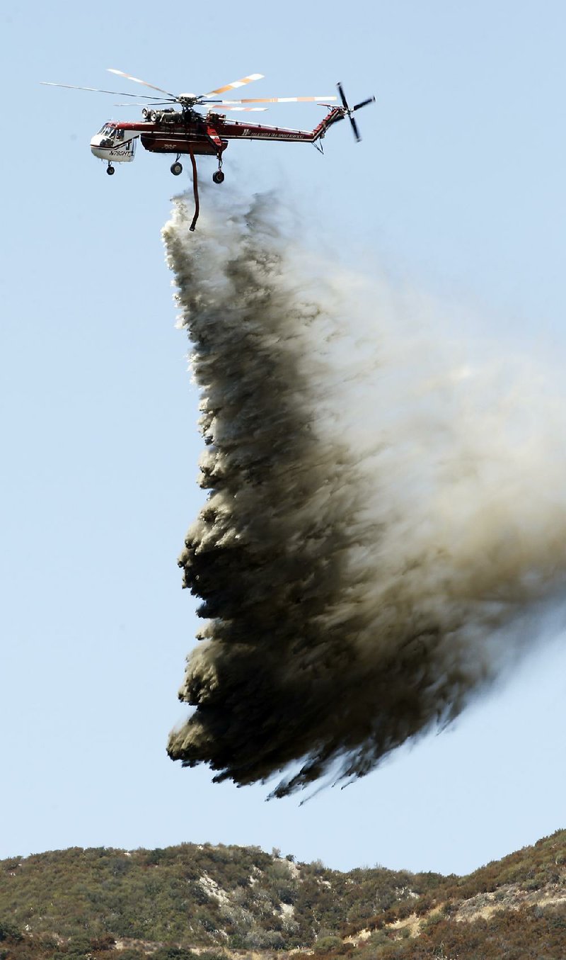 A helicopter drops fire retardant and water over a wildfire Wednesday near San Bernardino, Calif. About hundreds of firefighters have been called in to slow the blaze’s spread. 