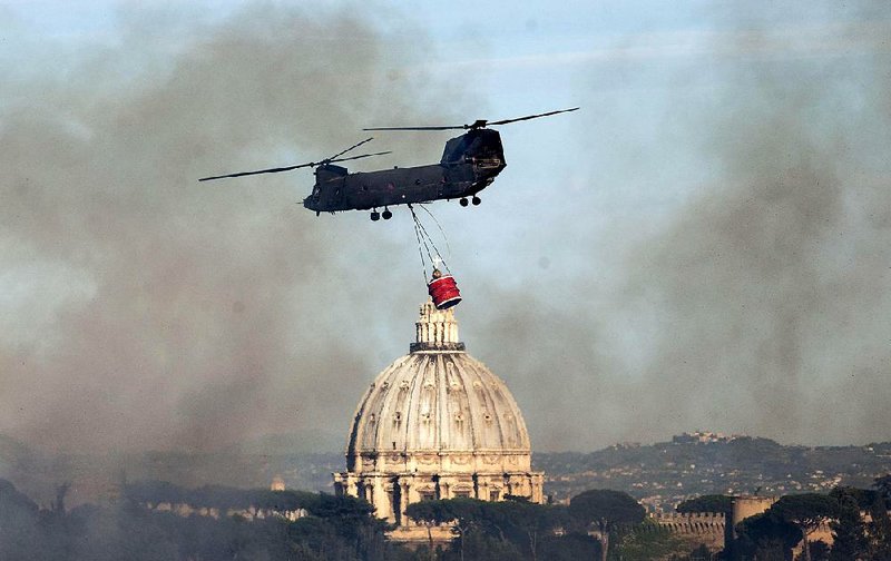 Smoke billows as a helicopter flies past the dome of St. Peter’s Basilica on its way to extinguish a fire that broke out in the Monte Mario hill area of Rome on Tuesday. 